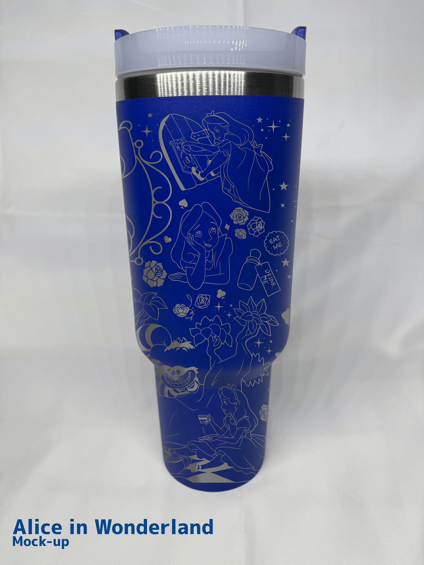 A blue 40oz engraved tumbler featuring an Alice in Wonderland-themed design. The engravings depict Alice peering through a door, sitting with a teacup, and surrounded by whimsical elements such as the Cheshire Cat, playing cards, roses, and "Eat Me" and "Drink Me" labels. The tumbler has a clear lid, stainless steel accents, and is set against a white fabric background. "Alice in Wonderland Mock-up" is written in blue text at the bottom left corner.